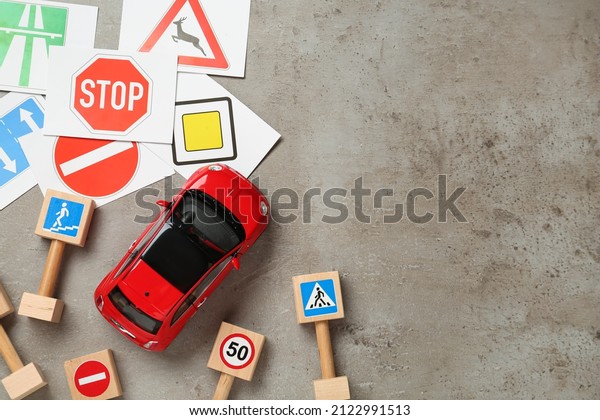 Many different road signs\
and toy car on grey background, flat lay with space for text.\
Driving school