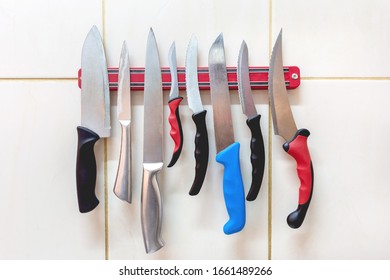 Many Different Types Of Knives, With Metal And Plastic Handles Are Attached To A Magnetic Bar On The Wall.