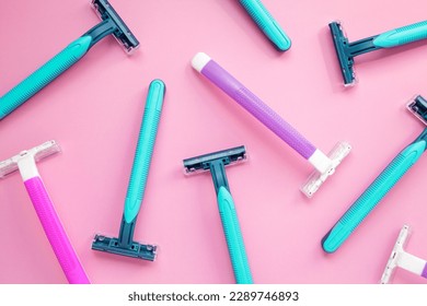 Many disposable purple and blue razors on a pink background. Colorful women and men hygiene accessories flat lay