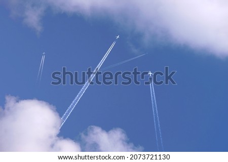 Many distant passenger jet planes flying on high altitude on clear blue sky leaving white smoke trace of contrail behind. Busy air transportation concept.
