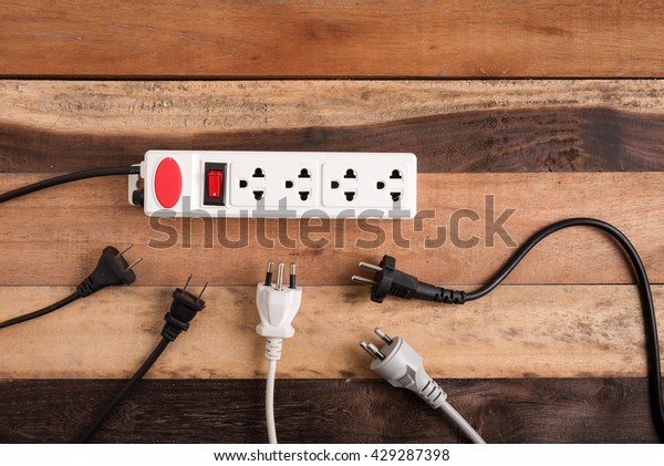 Many electrical plugs connected to a power\
strip or extension block on wooden\
table