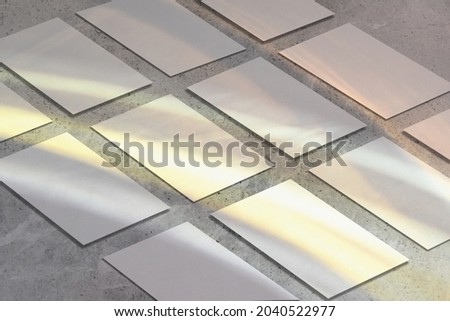 Many empty white horizontal rectangle a4 poster, business card or flyer mockups lying diagonally with overlay of rainbow light refraction caustic effect on gray concrete background. Isometric view