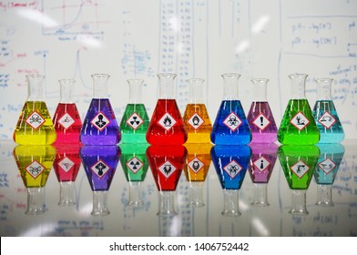 Many Of Erlenmeyer Flask With Colorful Liquid And Variety Type Of Chemical Hazard Warning Symbols Labels On Whiteboard With Chemical Learning Background.