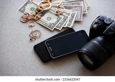 Many expensive golden jewerly rings, earrings and necklaces with big amount of US dollar bills close to smartphones and digital slr camera. Pawn shop concept