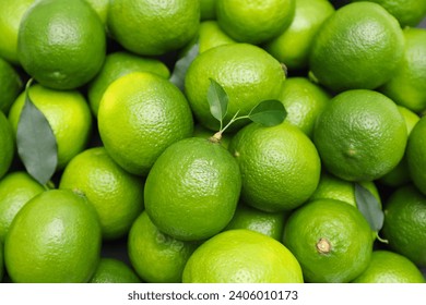 Many fresh limes with green leaves as background, top view