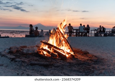 many friends enjoying a campfire in the beach at sunset - Powered by Shutterstock