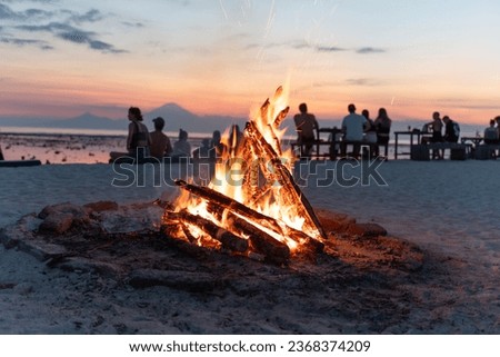 many friends enjoying a campfire in the beach at sunset
