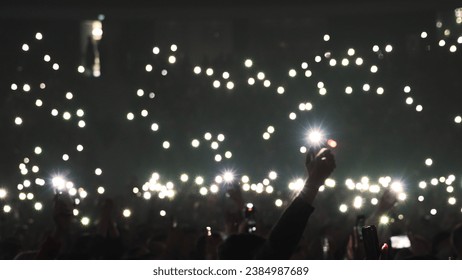 Many fun people lift hand up hold cell phone flash light. Fan crowd wave flashlights. Epic live music concert atmosphere. Big open air k pop arena. Cool night fest. Lot joy men hang out. Kpop chill.