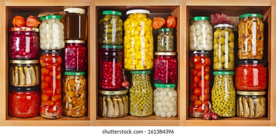 many glass bottles with preserved food set in wooden cabinet