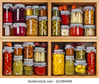 many glass bottles with preserved food in wooden cabinet