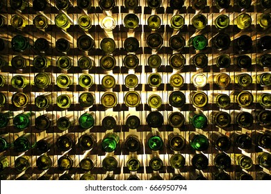 Many glass wine bottles on wine shelves with lighting. Interior in the restaurant. 
Color photo