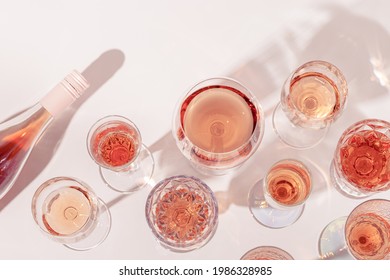 Many glasses of rose wine and bottle sparkling pink wine top view. Light alcohol drink for party. Flat lay on light table at summer day with shadows.  Stock fotografie