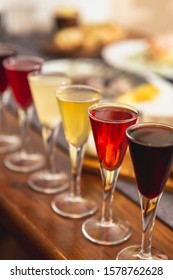 Many Glasses Of Shot Or Liqueur. Friends Drink Shot Or Liqueur And Cheers. Alcohol On Blurred Table Background. Party And Toast Concept.