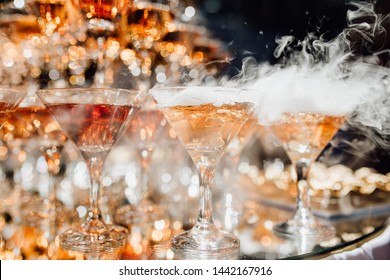 Viele Glaswaren mit rauchendem Cocktail-Getränk. Elegantes reichhaltiges Buffetdekor für Jubiläum von Geburtstag oder Hochzeit. Köstliche Getränke mit besonderer Wirkung für die Gäste. Catering und Restaurant Service