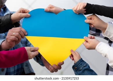 Many hands of different people holding a big heart with colors of Ukrainian flag. Freedom and support for Ukraine. Stop war.