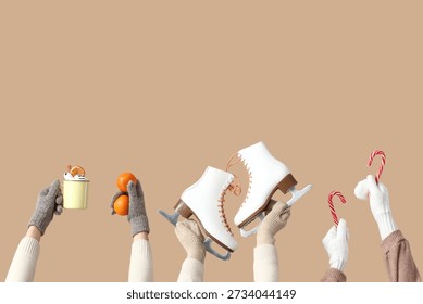 Many hands in different warm winter gloves with tangerines, cup of cocoa, skates and candy canes on beige background