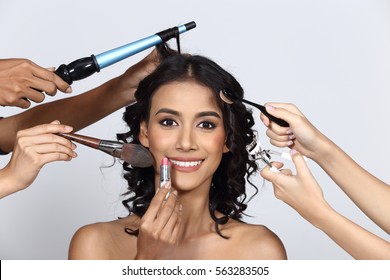 Many Hands Helping Tan Skin Woman Curl Black Hair To Be More Beautiful With Brush, Eye Curler, Lipstick, Hair Dresser, Studio Lighting Gray Background, Big Smile Teeth