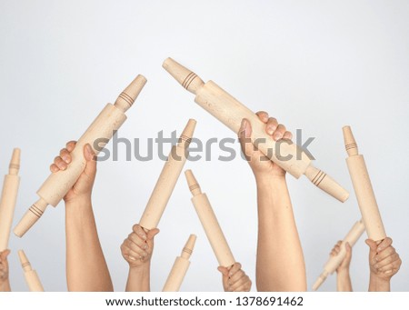 many hands raised up and holding kitchen wooden rolling pins on gray background, concept of riot