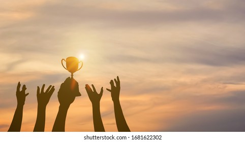 Many hands raised up. Winner is holding trophy cup in hand. Silhouettes of many hands in sunset. - Shutterstock ID 1681622302