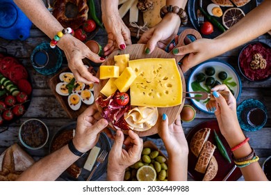 Many Hands Sharing Cheese And Bacon And Ham From The Serving Board. 