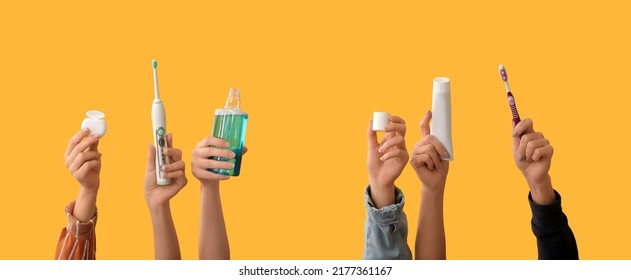 Many hands with toothbrushes, paste, mouth rinse and dental floss on yellow background - Powered by Shutterstock