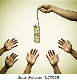 Many hands trying to get a dollar banknote hung on a fish hook - Shutterstock ID 310752059