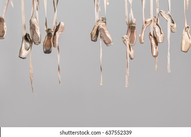 Many hanging beige ballet shoes on the gray background in the studio. Closeup. Horizontal.