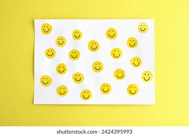 Many happy yellow smileys handpainted on white card on a bright yellow background - authentic image representing the concept of positive emotions, happiness, positive vibes, energy, motivation, fun