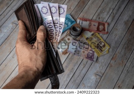 Many Hungarian forint (HUF) banknotes in a black wallet in a man's hand. Close-up. More money in the background