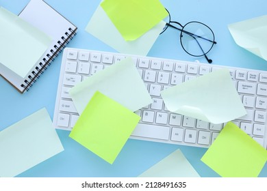 Many Ideas. Busy Work Schedule. Flat Lay Of The Workplace. White Keyboard. A Lot Of Sticky Note Paper On A Computer Keyboard With A Blue Paper Clip Background. Office Equipment.