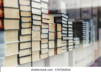 Many Identical Books Are Stacked On Top Of Each Other In A Glass Display Case Of A Bookstore.