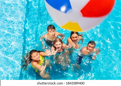 Many kids in swimming pool play with inflatable ball view from above reaching hands up