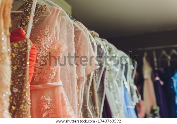 Many\
ladies evening gown long dresses on hanger in the dress rent shop\
for the wedding day. Dresses rental concept. Wedding dress for the\
wedding.selective focus.Ball gown rental\
concept.