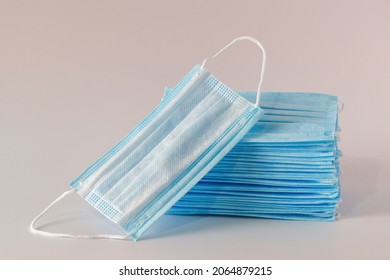 Many Medical Facial Three-layer Masks Are Stacked And One Mask Lies Next To The Light Background