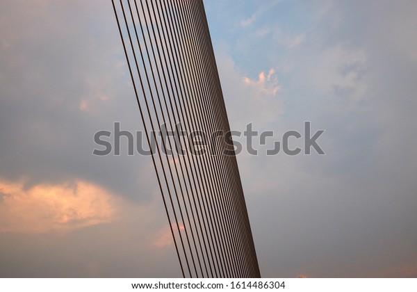 Many metal ropes of a suspension bridge cross\
the sky. Background.