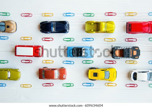 Many multi-colored toy cars on white\
background. The group of car toy on the road. Small cars on white\
table, top view with copy space. Traffic jam concept with multiple\
toy cars on a blackboard.