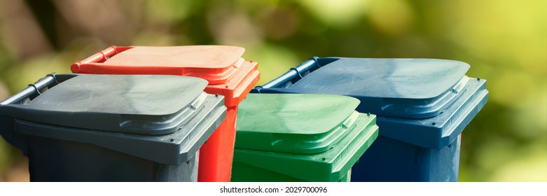 Many multicolored trash bin on green nature background. Separate and sorting garbage. Recycling and storage of waste for further disposal, trash sorting concept. Panoramic banner.
