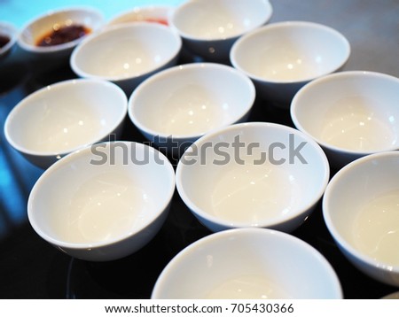 Many multiple small white empty ceramic melamine bowl cup stacked arrange altogether on Chinese banquet round table, with blurred sauce cups in the background, perspective view
