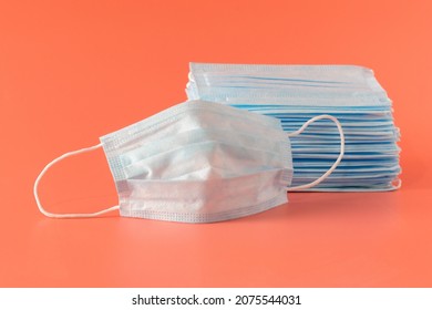 Many New Medical Facial Three-layer Masks Are Stacked And One Mask Lies Next To It On A Pink Background