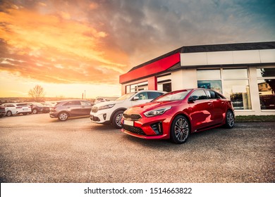 Many new stock cars standing in the front of modern car dealership building prepared for sale for customers/owners during sunny morning sunrise. - Powered by Shutterstock