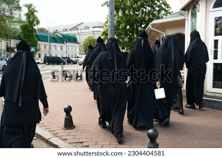 Many nuns in black dresses walking on the street, back view. 