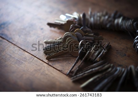 Many old keys placed on a well used old wooden desk with incoming light. Security and encryption, concept image.