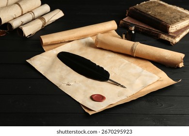Many old rolled scrolls, feather and inkwell on black wooden table, closeup
