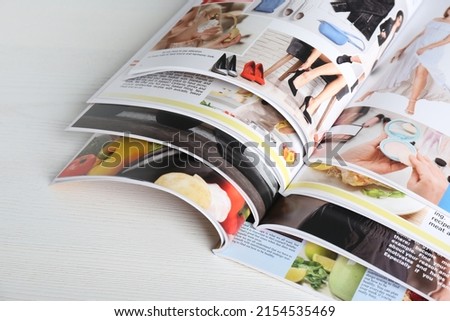 Many open magazines on white wooden table, above view