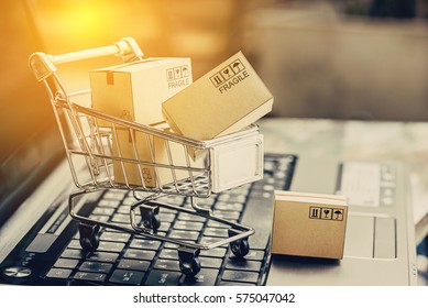 Many paper boxes in a small shopping cart on a laptop keyboard. Concepts about online shopping that consumers can buy things directly from their home or office just using a few clicks via web browser.