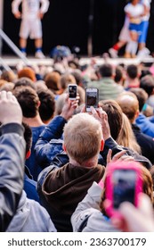 Many people at an outdoor concert using mobile phones to take photographs or videos - Shutterstock ID 2363700179