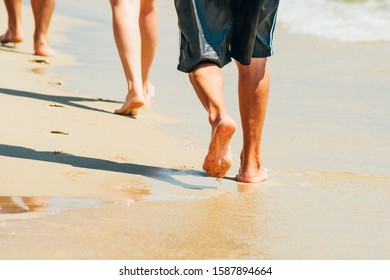 Many People Walking On The Beach. Peoples Moving Legs By The Sea