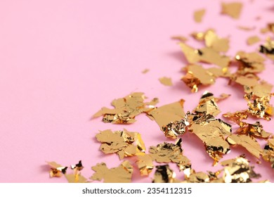 Many pieces of edible gold leaf on pink background, closeup. Space for text