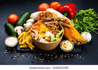Muchos trozos de ensalada de shawarma y César y papas fritas con verduras sobre un fondo negro