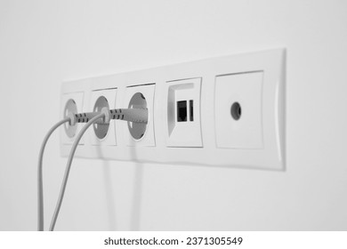 Many power sockets with plugs, ethernet and TV coax plates on white wall indoors - Shutterstock ID 2371305549
